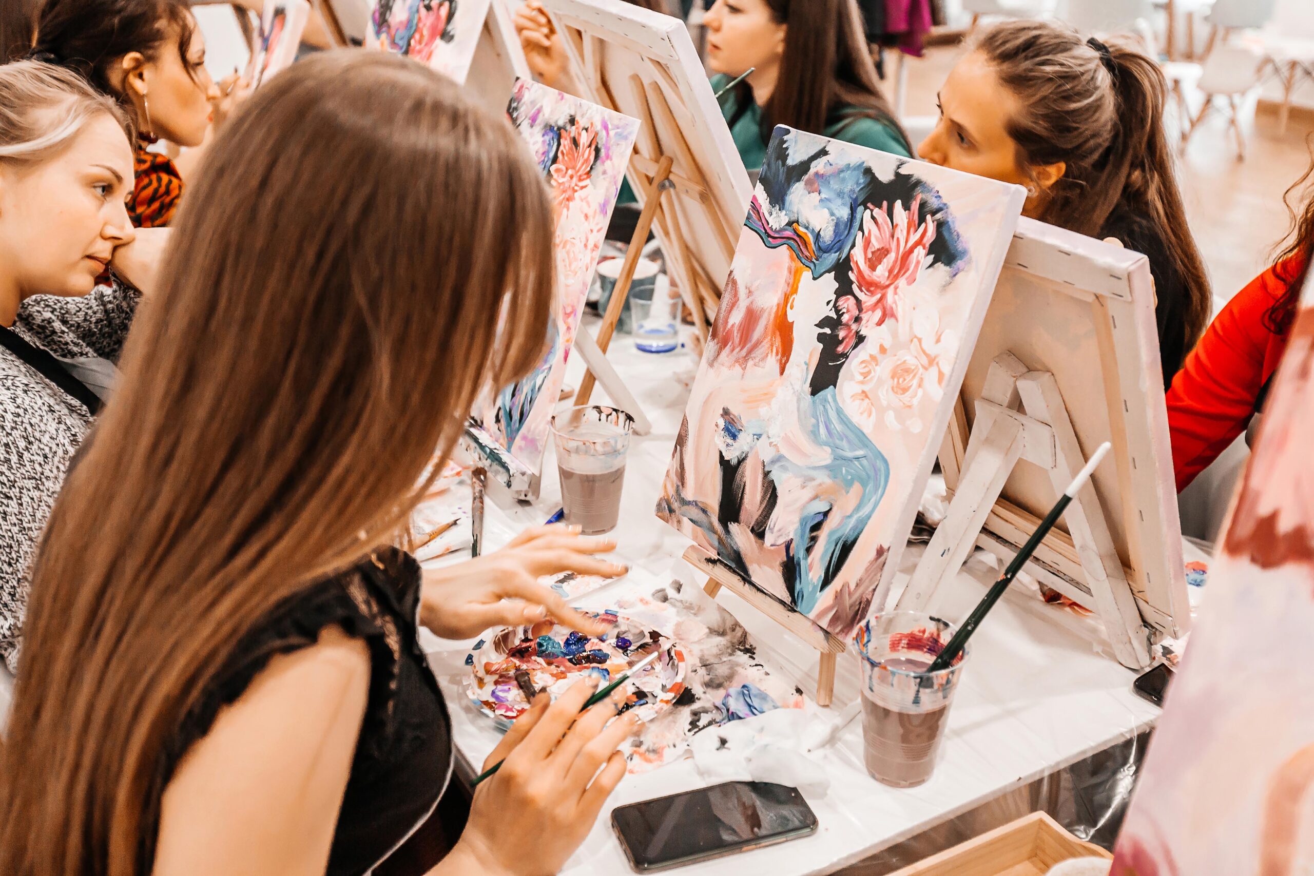 Young women paint with brushes on easels in art class. art school, creativity and people concept. selective focus